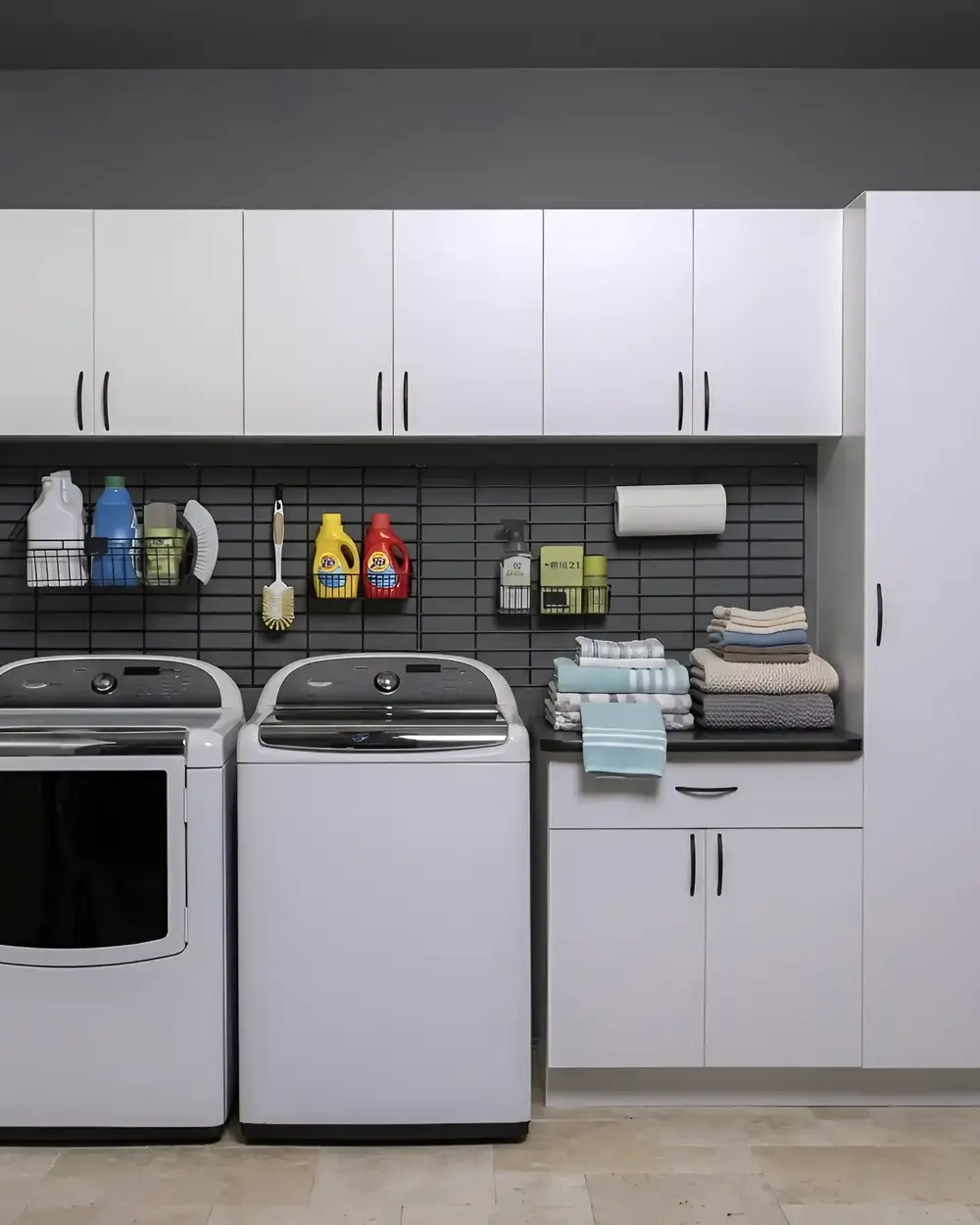 White laundry cabinets and a folding counter over a washer and dryer, with a dark tiled splashback