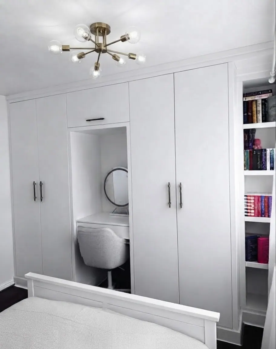A white floor-to-ceiling bedroom wardrobe with a built-in vanity niche, mirror and open bookshelves to the right
