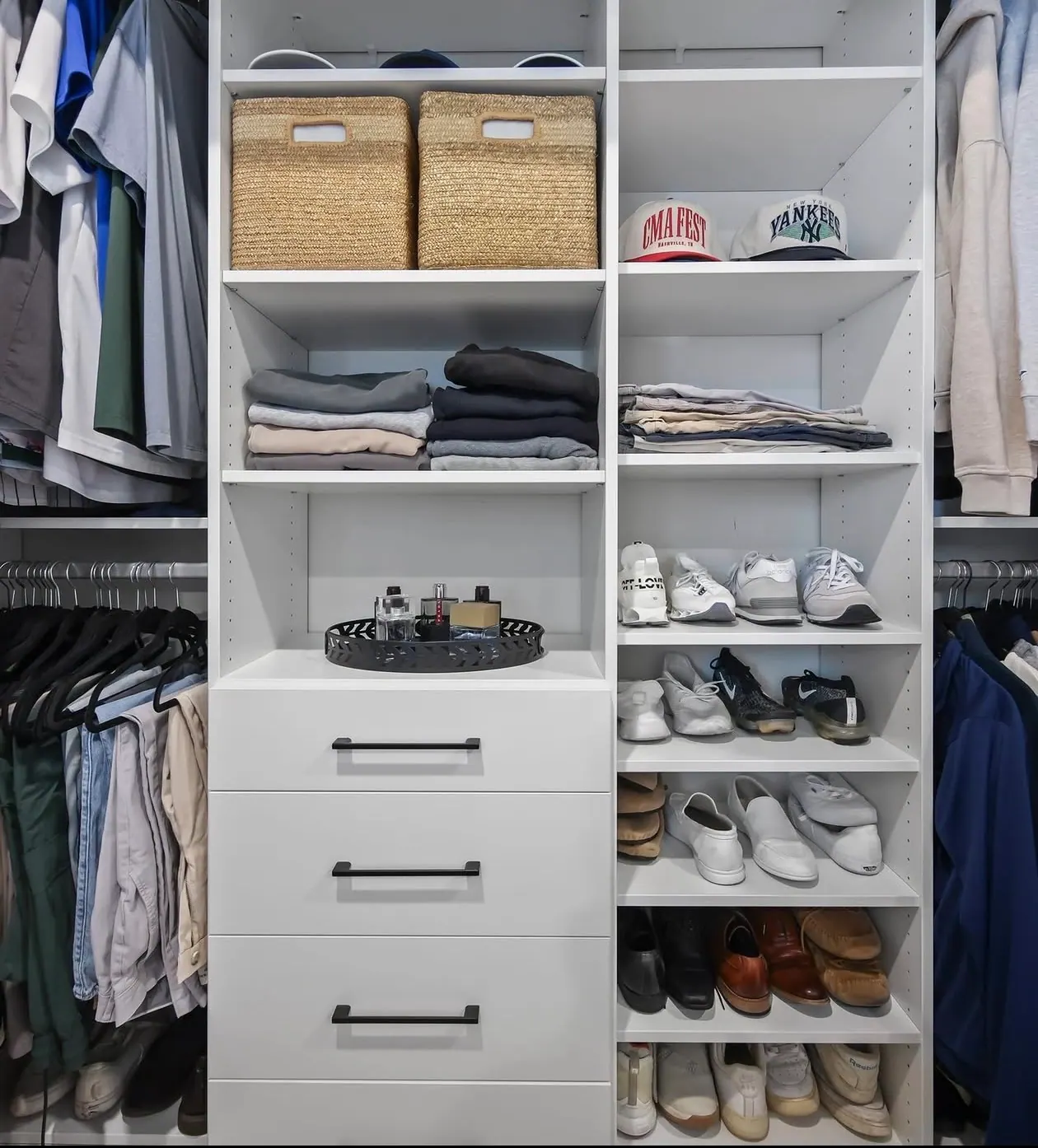 A white centre tower of open shelves over three drawers beside a column of shoe shelves, with hanging on either side