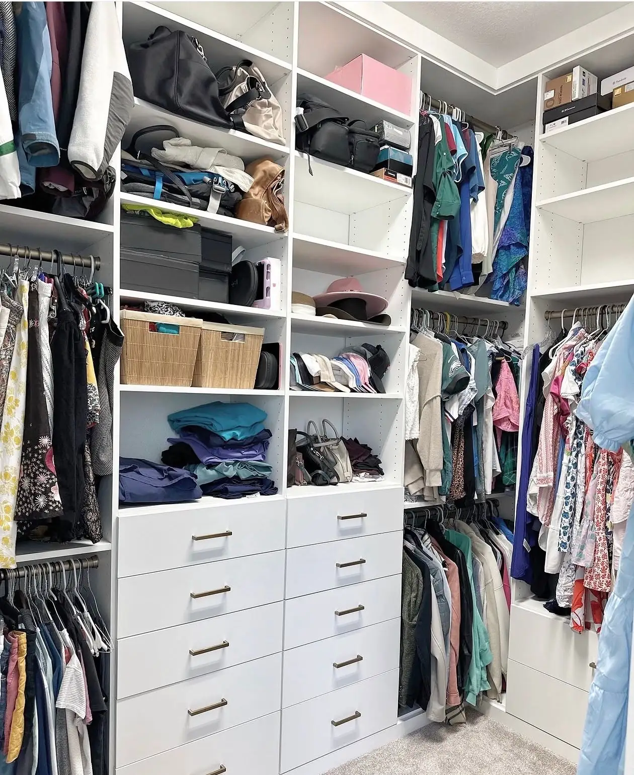 A white walk-in closet with two towers of drawers beside floor-to-ceiling shelving, and hanging rails down both side walls