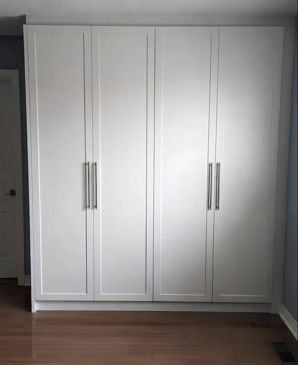 A floor-to-ceiling white wardrobe with four shaker doors and long bar handles in a bedroom
