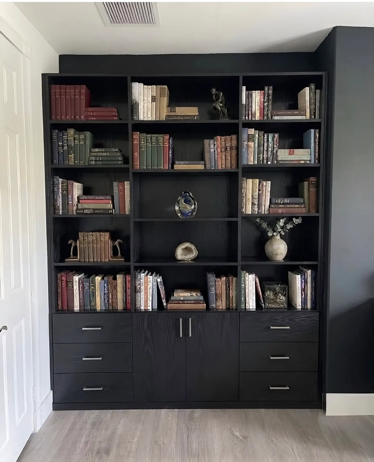 A black library wall with open shelving above a bank of drawers and a central cupboard, against a dark painted wall
