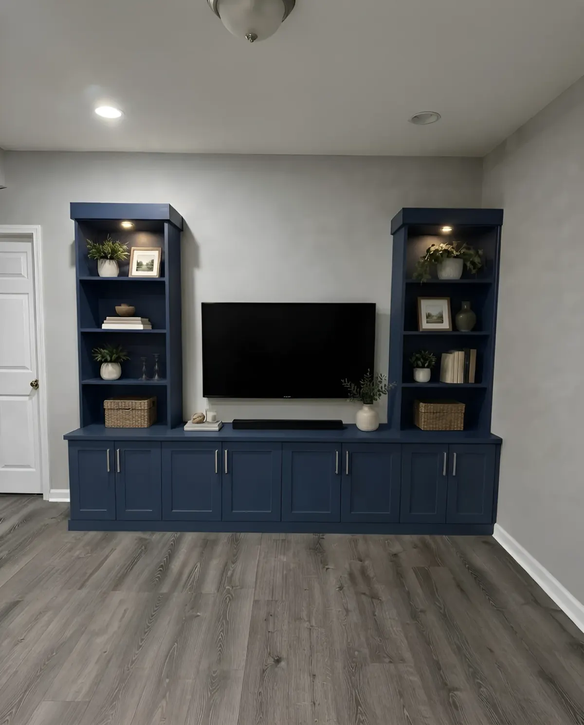 A navy media unit - two lit display towers flanking a wall-mounted screen, with a long run of shaker cupboards beneath
