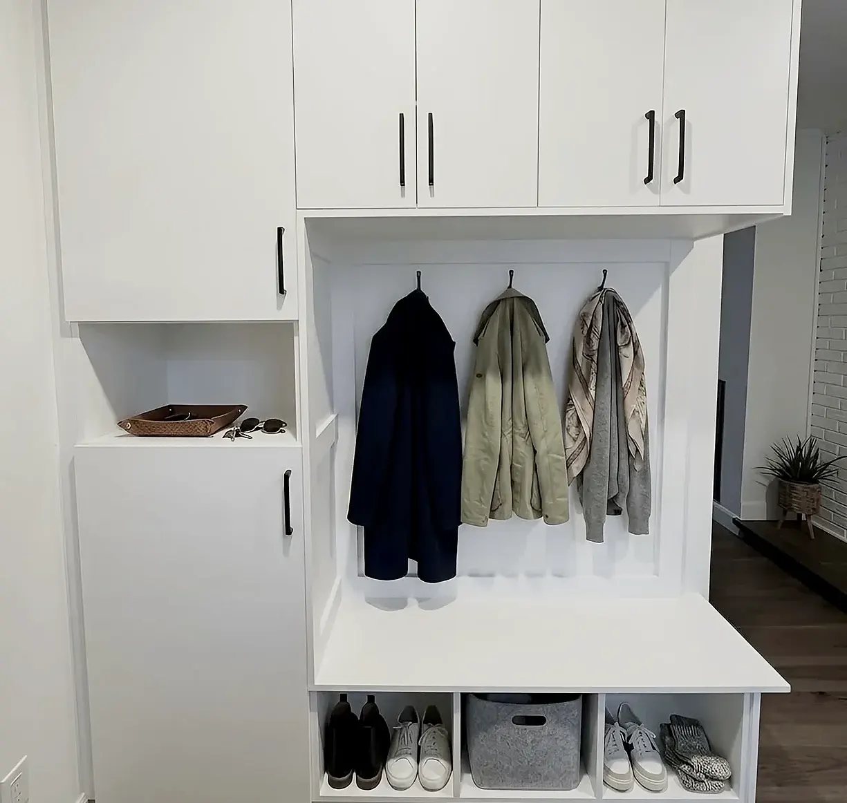The same mudroom seen whole — bench, shoe cubbies, coat hooks, a tall cabinet and closed uppers, fitted between a wall and a doorway