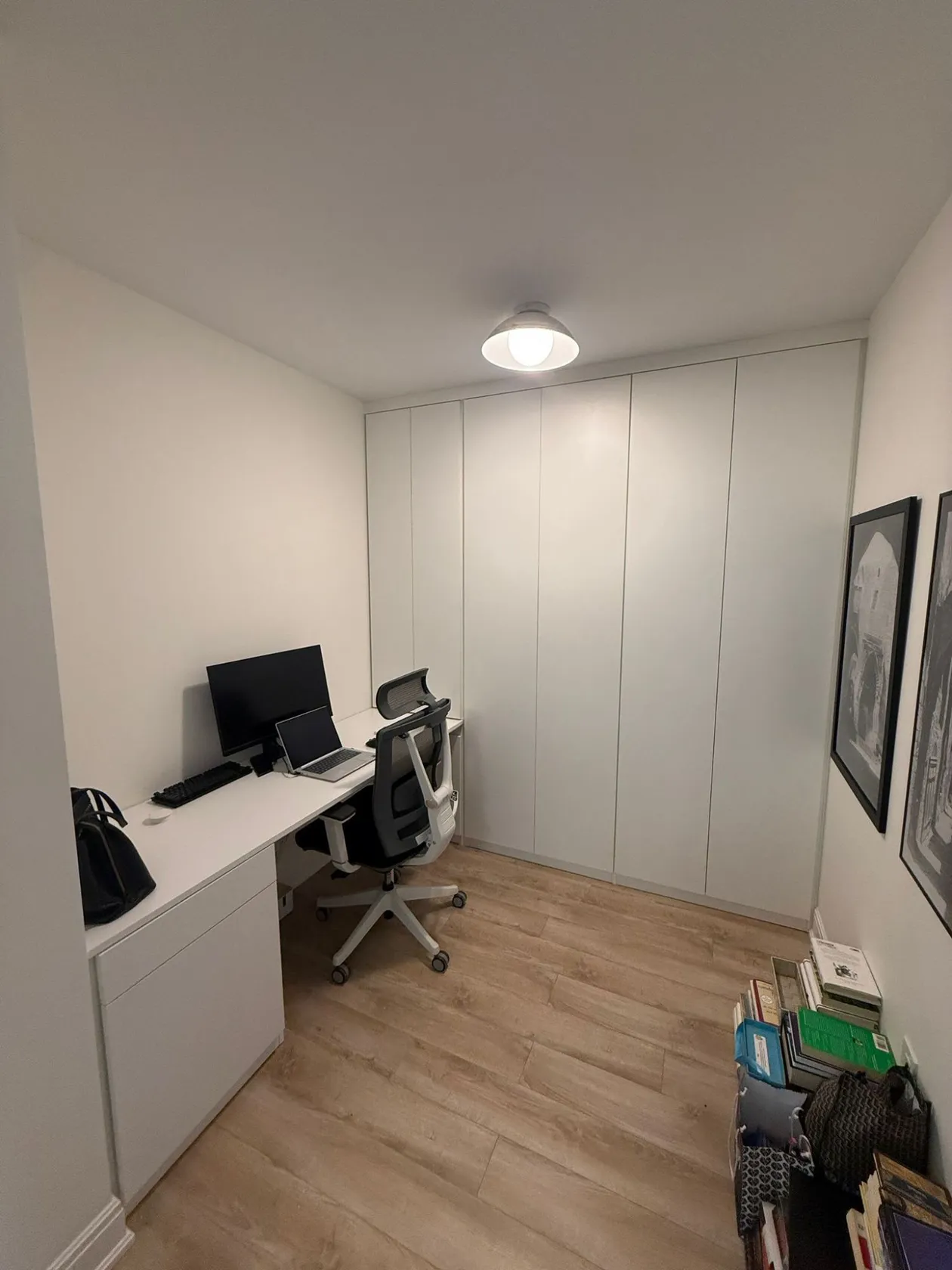 A small home office with a white desk run along one wall and a full-height wardrobe wall of handleless doors along the other